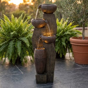 Rustic 33 inch tall 4-tier cascading outdoor water fountain with warm LED lights glowing on a cozy backyard patio at night.