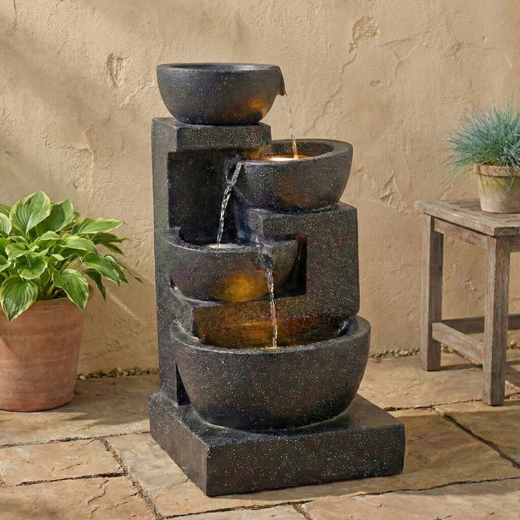 Terrazzo style LED water fountain with 29-inch 4-tier cascading bowls and stacked stones illuminating a cozy backyard patio at night.