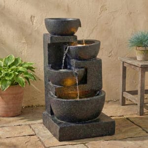 Terrazzo style LED water fountain with 29-inch 4-tier cascading bowls and stacked stones illuminating a cozy backyard patio at night.